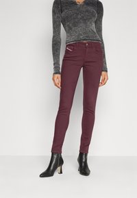 Jeans skinny burdeos con una textura suave, diseño de cinco bolsillos y costuras en contraste. Combinados con unas botas de tacón negro a la altura del tobillo.
