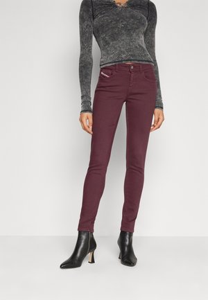 Jeans skinny burdeos con una textura suave, diseño de cinco bolsillos y costuras en contraste. Combinados con unas botas de tacón negro a la altura del tobillo.