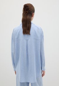 Camicia azzurra chiaro con righe bianche verticali. Presenta una spina dorsale, maniche lunghe e polsini abbottonati. Tessuto morbido.