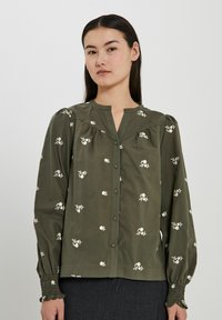 Olivgrön blus med vit blommönstring, knapplist fram, veckad detalj och smockade ärmslut. Mjuk bomullstyg.