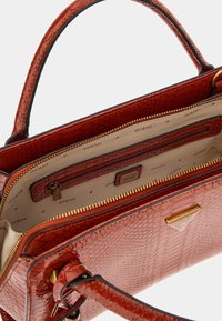 Rote, strukturierte Handtasche mit glänzender Oberfläche, ausgestattet mit einem Reißverschlussfach, goldenen Verzierungen und einem Logo-Schild. Das Innere beinhaltet Taschen.