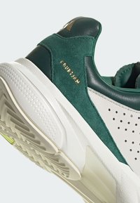 Zöld velúr és bőr sneaker perforált fehér részletekkel, aranyozott bélyegzett logóval és texturált gumitalppal.