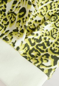 Tessuto in stampa leopardata verde e gialla con polsino a coste bianco. La texture è morbida, con motivi audaci e contrastanti in tutto il tessuto.