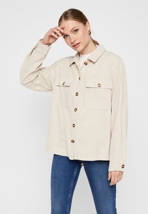 Beige corduroy-paita takki, jossa on kaksi etutaskua ja ruskeat napit. Siinä on kauluksessa oleva kaulus ja rento istuvuus.