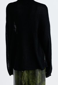 Zwarte gebreide trui met een losse pasvorm, voorzien van een open steekontwerp en ribbelstructuur. Inclusief een subtiele gekleurde accent aan de zijkant.