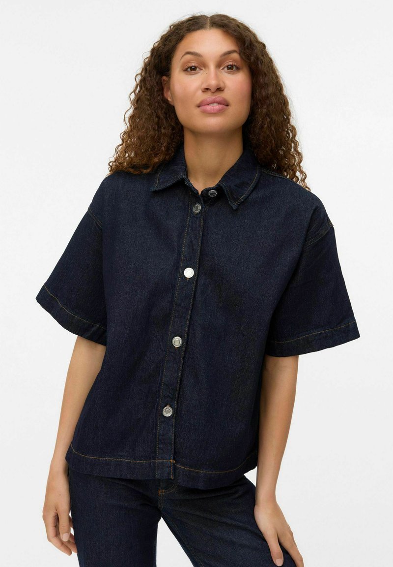 Mörk denimjacka med kort ärm, krage och silverfärgade knappar. Har kontrasterande sömmar och en rak fålldesign.