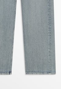 Jambes de pantalon en denim bleu clair montrées à plat avec des coutures visibles et des ourlets droits sur un fond blanc.
