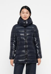 Veste matelassée marine avec un col haut et une fermeture éclair. Présente des motifs matelassés, des poches latérales et une finition brillante.