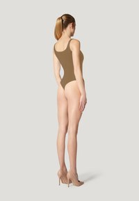 Bodysuit marrone con spalline larghe, design aderente e aperture delle gambe alte, abbinato a tacchi nudi, su uno sfondo neutro.