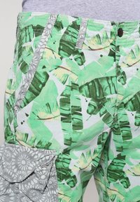 Zielone szorty cargo z nadrukiem liści bananowca, jasnoszare kwiatowe kieszenie i zapięcie na guzik. Wykonane z przewiewnego materiału.
