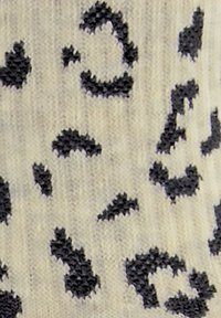 Wzorzysta dzianina z beżowym tłem i czarnymi plamami przypominającymi lamparta, o miękkiej fakturze i różnorodnych kształtach plam.