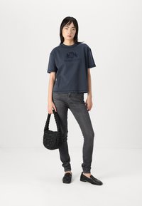 Marineblå bomulds t-shirt med korte ærmer og rund halsudskæring, med et tonalt logo. Sammen med sorte jeans og en struktureret sort taske.