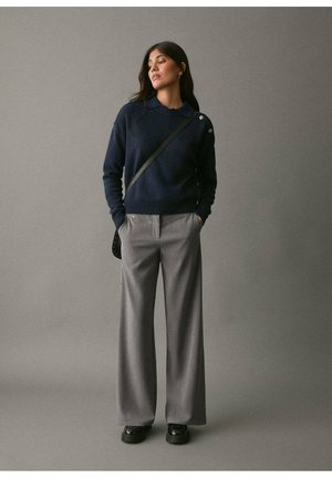 Pull en mailles bleu marine avec un col, associé à un pantalon large gris clair. Sac bandoulière noir et chaussures noires à finition lisse.