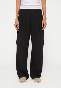 Schwarze, weite Cargo-Hosen mit vorderen Falten, zwei Seitentaschen und einem sicheren Knopfverschluss. Hergestellt aus einem glatten, leichten Stoff.