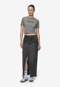 Grå kort t-skjorte med svart logo, kombinert med et langt svart denimskjørt med splitt foran og frynset kant, fullført med grå sneakers.