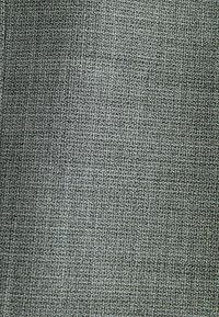 Primer plano de tela gris con un patrón texturizado a pequeña escala tejido de manera apretada, creando una apariencia de superficie densa y uniforme.