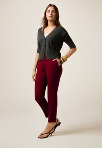 Grijze kortemouw cardigan, bordeaux gepelde broek en zwarte sandalen met bandjes. Gladde texturen en getailleerde stijlen creëren een moderne outfit.