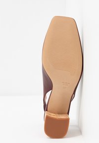 Chaussure à talon en cuir marron avec dos ouvert et côtés découpés. Talon en liège, finition lisse et semelle en caoutchouc avec rainures horizontales.