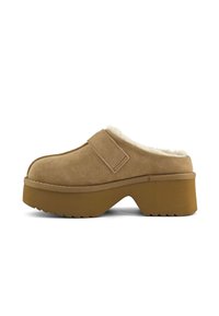 Sabots en suédine marron avec une surface texturée, doublure en fausse fourrure et une semelle en caoutchouc épaisse et crantée. Comprend une sangle Velcro sur le cou-de-pied.