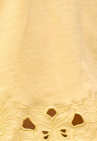 Tissu jaune avec broderies florales et détails découpés le long du bord d'un vêtement.