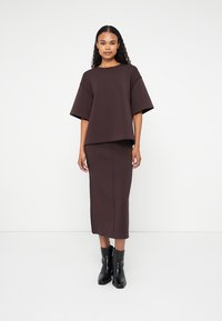 Completo composto da top aderente marrone e gonna lunga, realizzato in tessuto strutturato, con un design semplice e maniche ampie, abbinato a stivaletti neri.