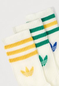 Trys poros ribotų, iki kulkšnių ilgio kojinių balta spalva su geltonais, žaliais ir mėlynais dryžuotais akcentais ir atitinkamu logotipu ant apvado.