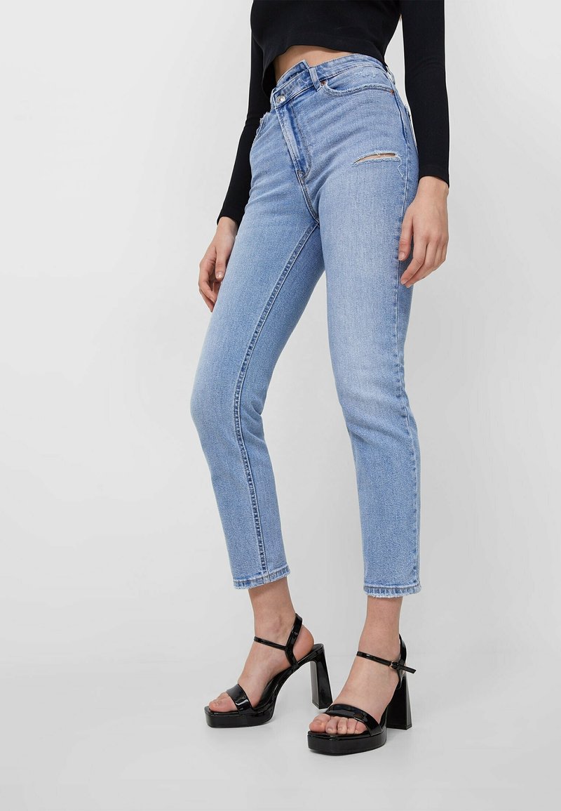 Ljusblå högmidjade jeans med smal passform och lätt slitningar, tillsammans med svarta lackläderssandaler med platå.