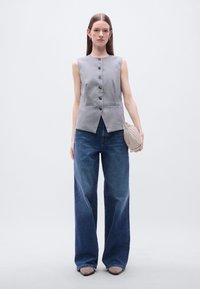 Γκρι αμάνικη μπλούζα με έξι κουμπιά και δύο μπροστινές τσέπες, συνδυασμένη με ψηλόμεσα, φαρδιά μπλε τζιν και τσάντα σε ουδέτερο τόνο.