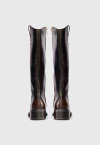 Une paire de bottes en cuir marron foncé, hautes, avec des fermetures éclairs et des tirettes, vues de l'arrière sur un fond clair.