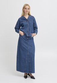 Tvådelad denim-outfit med en knäppt skjorta med krage och en lång kjol. Båda delarna har en medel wash med synliga sömnadsdetaljer.