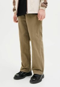 Pantaloni khaki larghi in cotone, con tasche laterali, dettagli cuciti e una vestibilità dritta, abbinati a stivali neri con lacci.