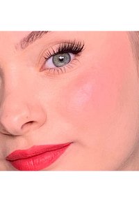 Close-up van een gezicht met een heldere roze lipkleur, lichte blos, volle wimpers en groene ogen met een gladde, lichte teint.