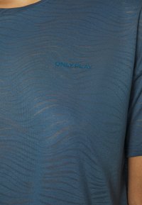Niebieska koszulka sportowa z krótkim rękawem i okrągłym dekoltem w wzór fal. Na piersi znajduje się tekst "ONLY PLAY" w kontrastującym kolorze.
