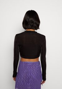 Svart cropped långärmad topp med en slät yta, tillsammans med en lila kjol med vågigt mönster och knyt-detaljer på sidan.