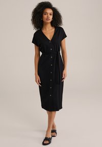 Abito midi nero con maniche corte, scollatura a V, bottoni frontali e una cintura abbinata. Tessuto morbido con silhouette aderente.