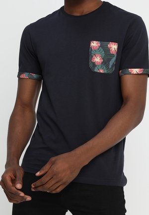 Navy blue t-shirt with floral pocket design and patterned cuffs. Short sleeves, crew neck, fitted shape, made of soft cotton fabric.