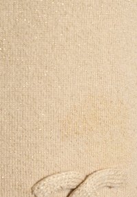 Gros plan sur un tissu tricoté beige avec des fils scintillants subtils et un détail texturé de tricot au bas.