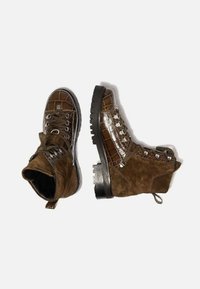 Botas marrones que combinan cuero brillante con patrón de cocodrilo y gamuza texturizada, con ojales de metal y una suela negra robusta.