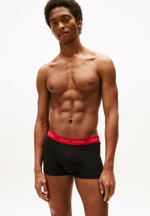 Boxer-briefs noirs avec un logo TOMMY HILFIGER rouge sur la ceinture. Le tissu semble lisse et extensible, s'ajustant étroitement au corps.