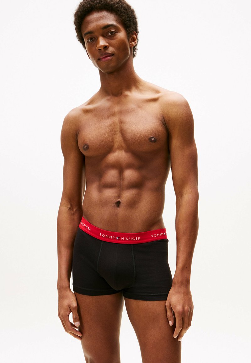 Schwarze Boxershorts mit einem roten TOMMY HILFIGER-Logo am Bund. Der Stoff wirkt glatt und dehnbar und passt eng am Körper.