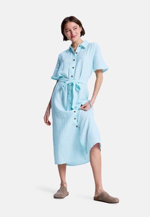 Jasnoniebieska sukienka koszulowa w paski z krótkimi rękawami, guziki z przodu i wiązanym paskiem w talii. Posiada długość do połowy uda i miękką fakturę.