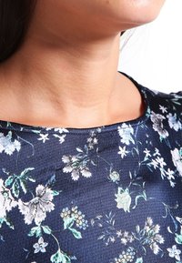 Haut à motifs floraux avec un fond marine, un col plongeant et un tissu texturé agrémenté de fleurs bleues et blanches.