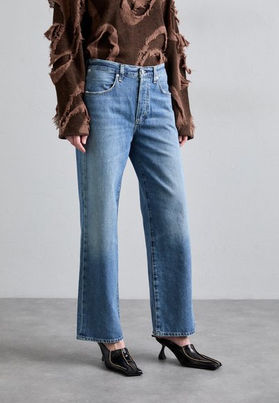 Lyseblå vide jeans med falmet vask, med klassisk fem-lomme design, brukt med en brun slitt genser og svarte sko med hæl.