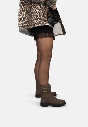 Bruine enkelbotten met een zijgesp, gecombineerd met zwarte shorts met kant en doorzichtige zwarte panty’s, onder een overshirt met luipaardprint.