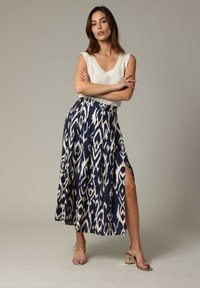 Jupe maxi à motifs bleu marine et crème avec une fente sur le côté, fabriquée dans un tissu lisse, associée à un haut en tricot crème texturé et des talons métalliques.