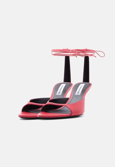 Κόκκινα γυναικεία ψηλοτάκουνα σανδάλια με ανοιχτά δάχτυλα, λουριά για δέσιμο στον αστράγαλο και μαύρες εσωτερικές σόλες με την ετικέτα Victoria Beckham.