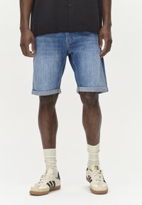 Denimske kratke hlače v svetlo modri barvi z zavihkom, v kombinaciji s kremnimi nogavicami in retro športnimi copati z črnimi črtami.