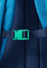 Fivela de plástico verde com alça de mochila em tecido azul e marinho, apresentando material texturizado e um design de strap ajustável e seguro.