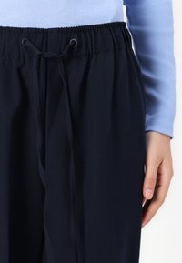 Pantalons bleu marine avec une taille à cordon, présentant une texture lisse et une coupe décontractée. Pas de motifs visibles ni de détails en métal.