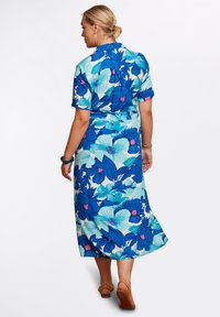 Blommig midi-klänning med ett livligt blått och grönt mönster, korta ärmar, krage och en avslappnad passform, matchad med bruna sandaler.